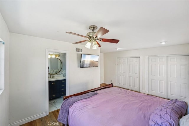 bedroom featuring two closets, visible vents, ensuite bath, wood finished floors, and baseboards