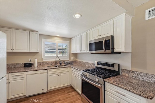 kitchen featuring light wood finished floors, visible vents, appliances with stainless steel finishes, white cabinetry, and a sink