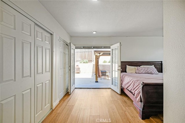 bedroom with access to exterior, a textured ceiling, french doors, light wood-style floors, and two closets