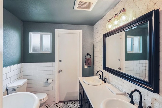 full bath featuring a wainscoted wall, a sink, visible vents, and tile walls