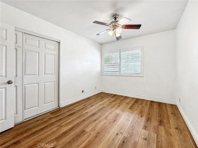 unfurnished bedroom with a closet, wood finished floors, a ceiling fan, and baseboards