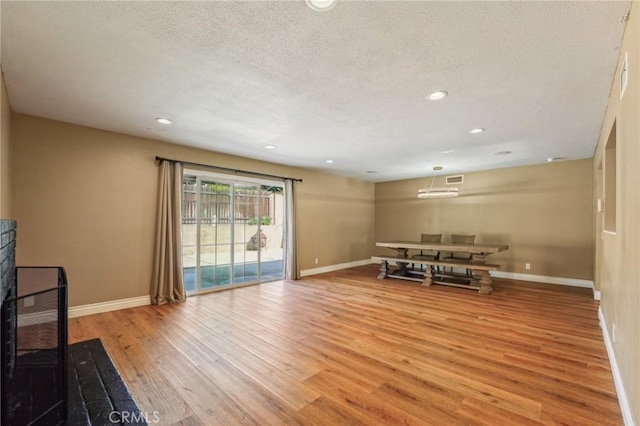 living room featuring light wood finished floors, baseboards, a textured ceiling, and a stone fireplace