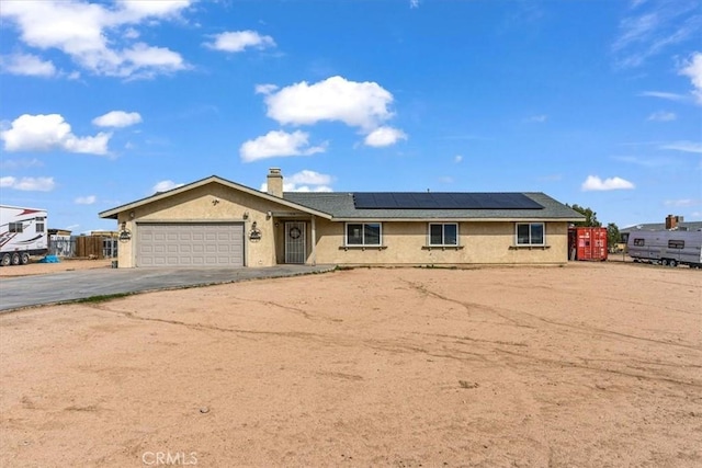 ranch-style house with driveway, a garage, a chimney, roof mounted solar panels, and stucco siding