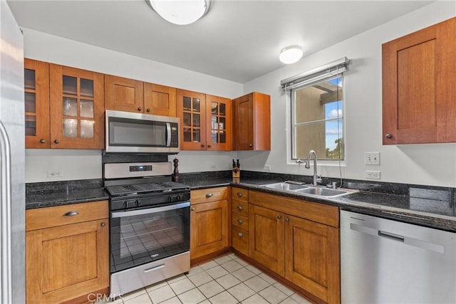 kitchen featuring light tile patterned floors, brown cabinetry, glass insert cabinets, appliances with stainless steel finishes, and a sink