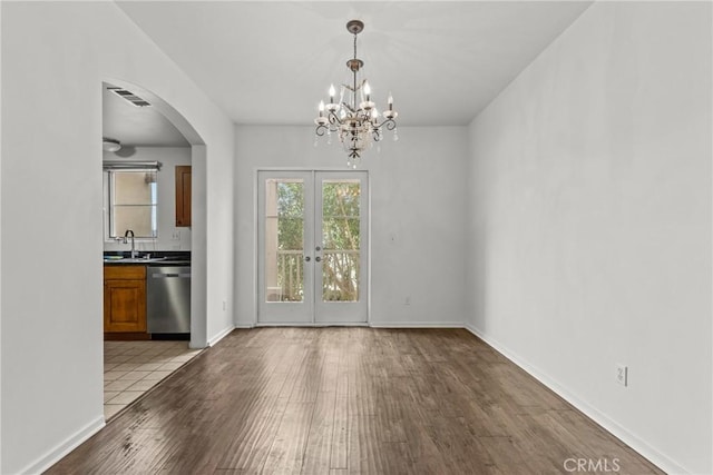 unfurnished dining area with baseboards, arched walkways, wood finished floors, and french doors