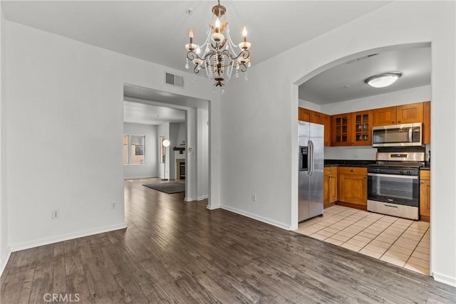 kitchen featuring arched walkways, appliances with stainless steel finishes, brown cabinetry, and visible vents