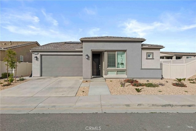 prairie-style home with a garage, fence, concrete driveway, roof mounted solar panels, and stucco siding