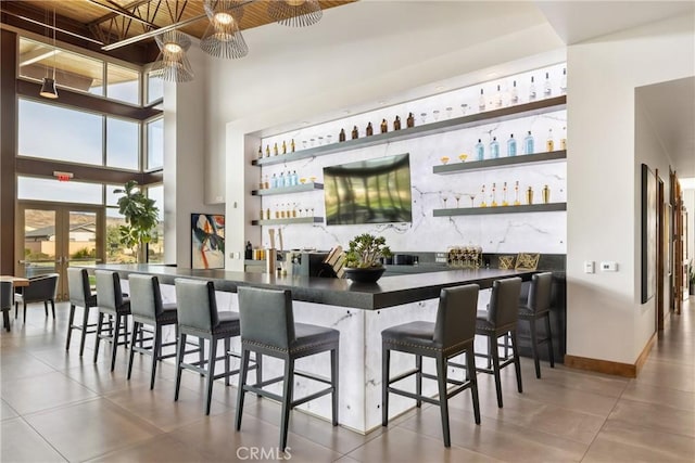 bar featuring baseboards, a high ceiling, and indoor wet bar