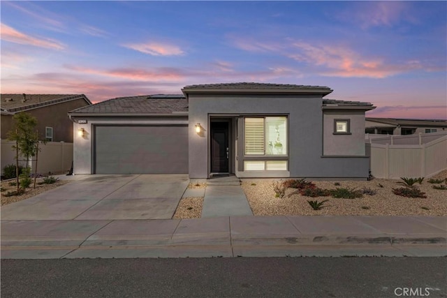 view of front of house featuring solar panels, stucco siding, concrete driveway, fence, and a garage