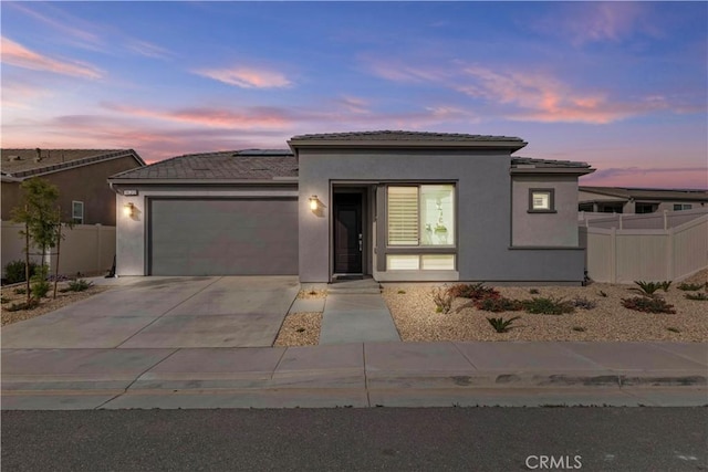 view of front of home featuring fence, a garage, concrete driveway, solar panels, and stucco siding