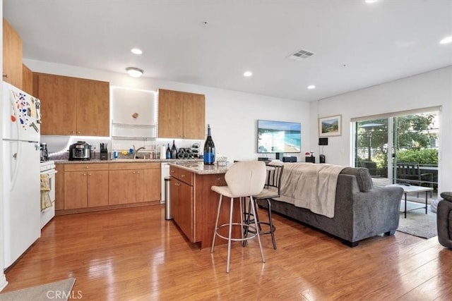 kitchen featuring white appliances, a kitchen island, visible vents, open floor plan, and light wood-type flooring