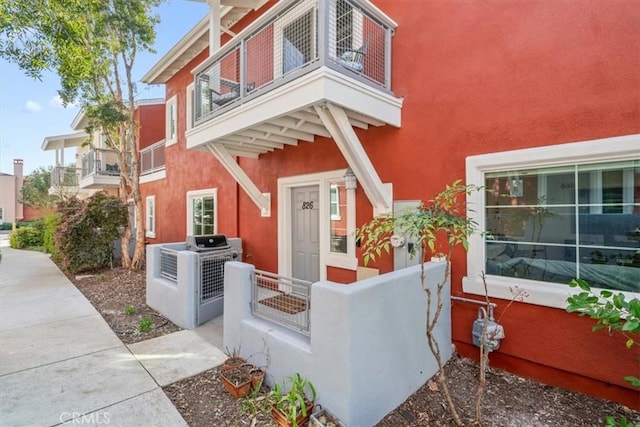 entrance to property featuring fence, a balcony, and stucco siding