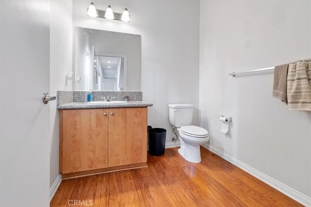 half bathroom featuring toilet, baseboards, wood finished floors, and vanity