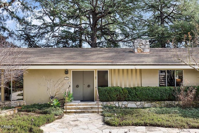 view of front of property with a tiled roof, a chimney, and stucco siding