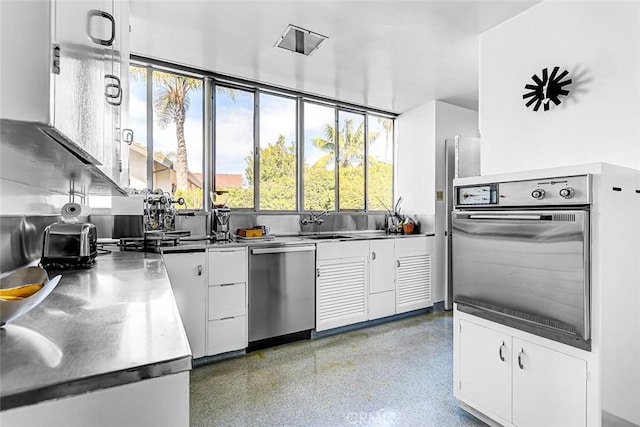 kitchen with stainless steel counters, appliances with stainless steel finishes, white cabinets, a sink, and speckled floor