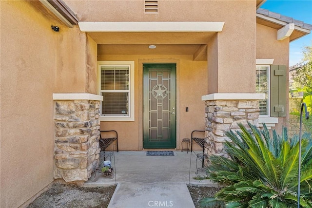 property entrance with stone siding, visible vents, and stucco siding