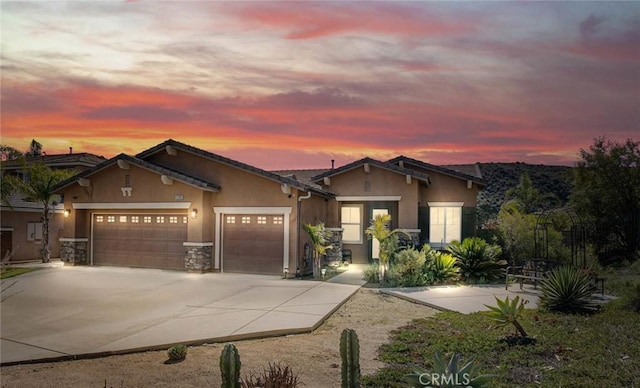 view of front facade featuring driveway, stone siding, an attached garage, and stucco siding