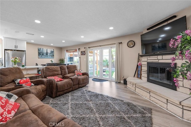 living room with a textured ceiling, a stone fireplace, light wood-type flooring, and recessed lighting