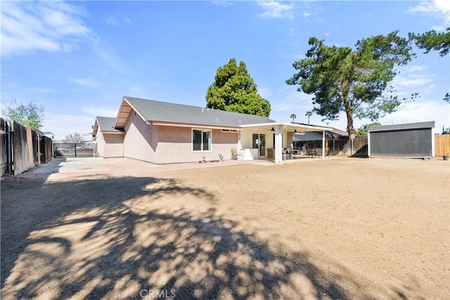 back of property with fence, a storage unit, an outdoor structure, and stucco siding