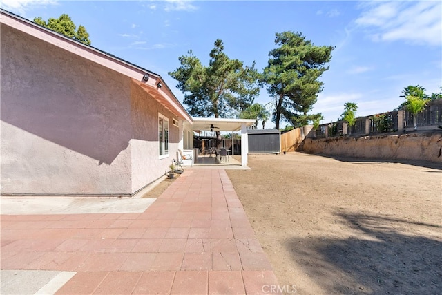 view of yard featuring a storage shed, a fenced backyard, ceiling fan, and a patio