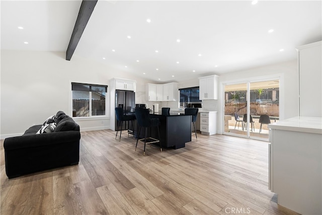 kitchen featuring vaulted ceiling with beams, white cabinetry, a kitchen breakfast bar, open floor plan, and a center island