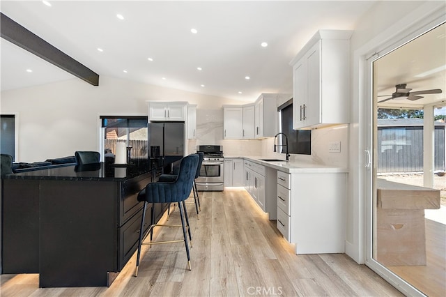 kitchen with vaulted ceiling with beams, stainless steel appliances, white cabinetry, a kitchen island, and a sink