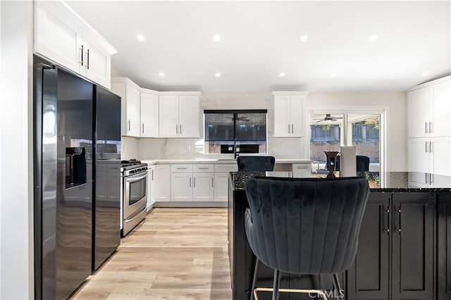 kitchen with light wood-style floors, white cabinets, stainless steel range with gas cooktop, dark stone counters, and black refrigerator with ice dispenser