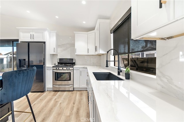 kitchen with light wood-style flooring, stainless steel appliances, a sink, white cabinets, and light stone countertops