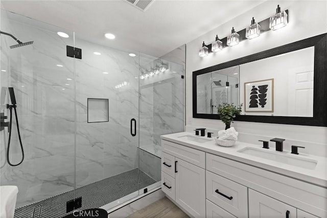 full bath featuring visible vents, a sink, a marble finish shower, and double vanity