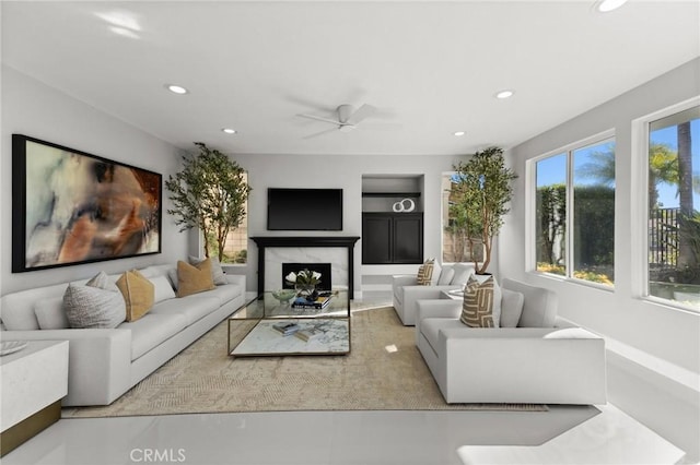 living area featuring built in shelves, recessed lighting, ceiling fan, and a premium fireplace