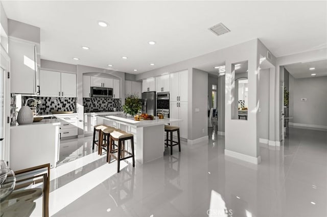 kitchen featuring appliances with stainless steel finishes, a kitchen breakfast bar, a center island, light countertops, and white cabinetry