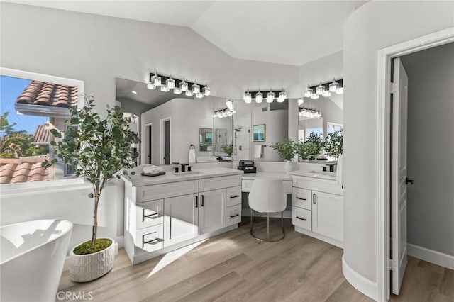 bathroom featuring baseboards, lofted ceiling, a soaking tub, wood finished floors, and vanity