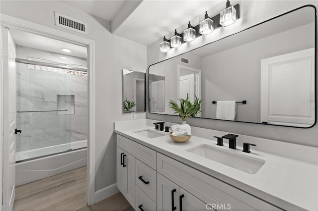 bathroom with visible vents, bath / shower combo with glass door, a sink, and wood finished floors