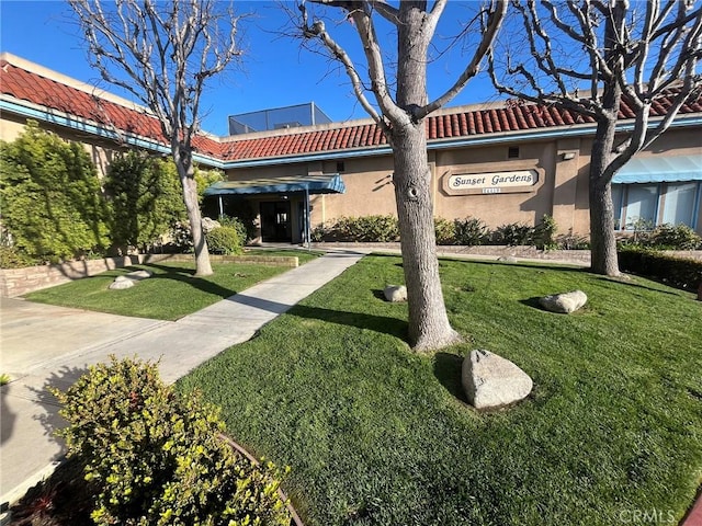 view of front of house with a tiled roof, a front yard, and stucco siding