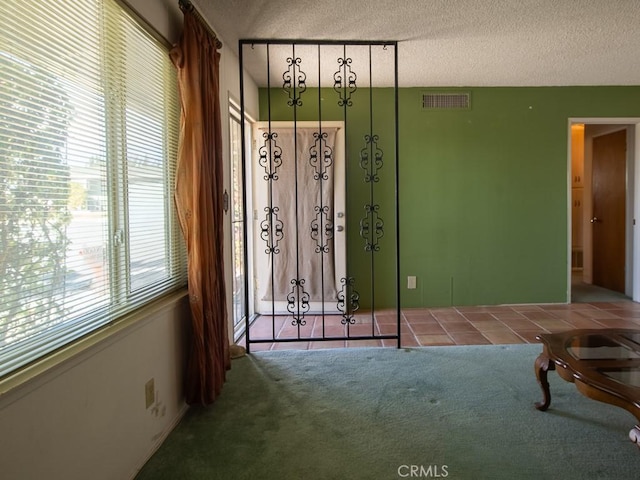 tiled spare room with carpet floors, visible vents, and a textured ceiling