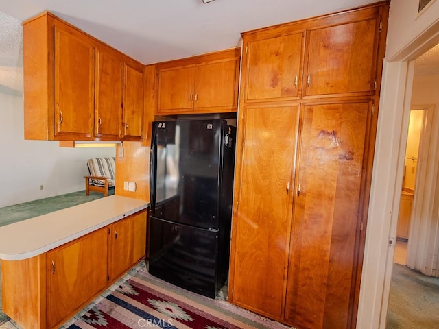 kitchen with brown cabinetry, visible vents, light countertops, and freestanding refrigerator