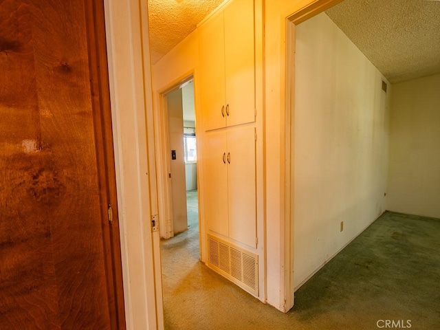 hall featuring a textured ceiling, carpet, and visible vents