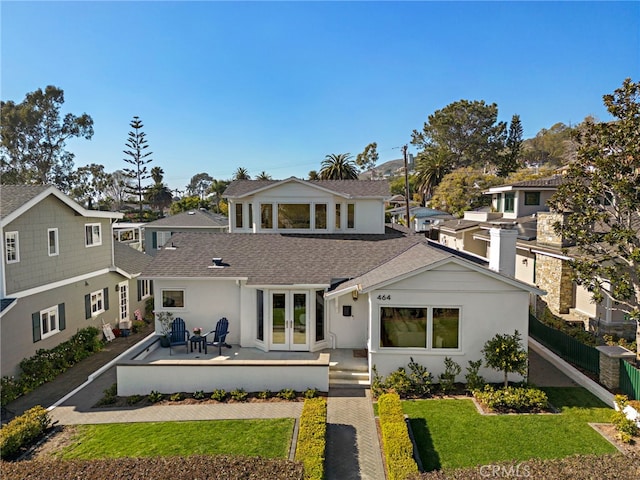 back of property with a residential view, roof with shingles, a lawn, and a patio