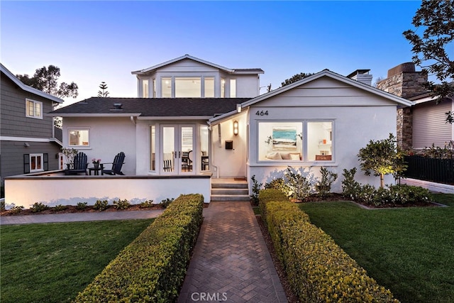 view of front facade with a yard, french doors, and stucco siding