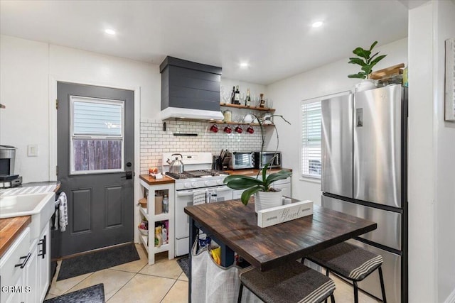 kitchen with white range with gas cooktop, wall chimney exhaust hood, butcher block countertops, freestanding refrigerator, and backsplash