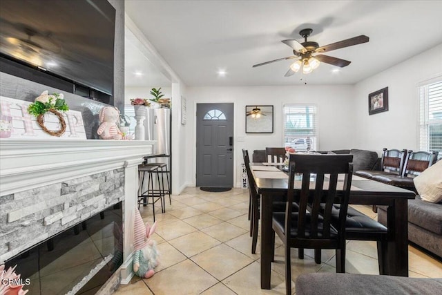 dining room featuring light tile patterned floors, a ceiling fan, a wealth of natural light, and a stone fireplace