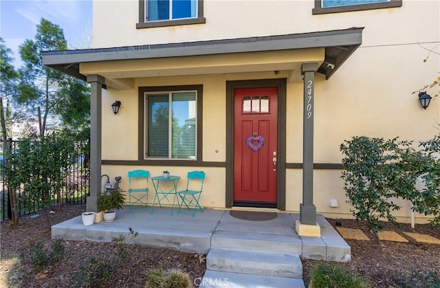 doorway to property with covered porch, fence, and stucco siding