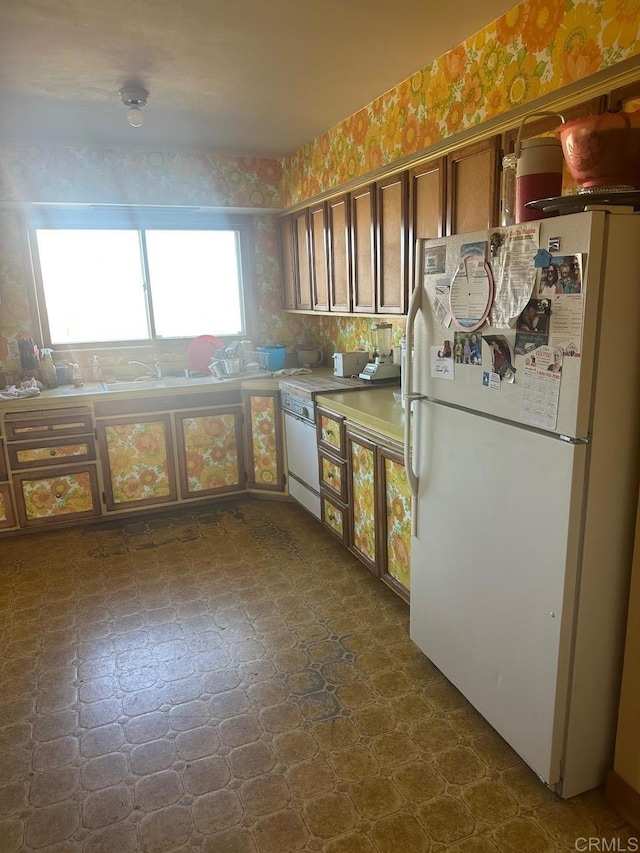 kitchen with freestanding refrigerator, brown cabinets, dark floors, and wallpapered walls