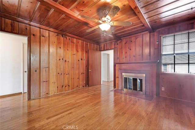 unfurnished living room featuring light wood finished floors, wooden walls, a ceiling fan, wood ceiling, and a fireplace with flush hearth