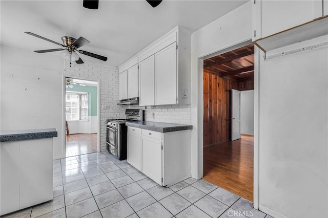 kitchen featuring white cabinets, dark countertops, stainless steel electric stove, under cabinet range hood, and light tile patterned flooring