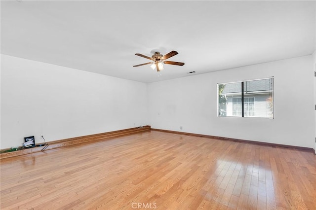 spare room featuring light wood finished floors, a ceiling fan, and baseboards