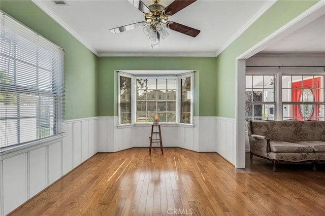 unfurnished room featuring light wood-style floors, ceiling fan, ornamental molding, and wainscoting