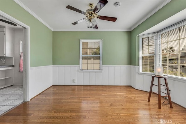 empty room featuring a wainscoted wall, light wood-style flooring, and a healthy amount of sunlight