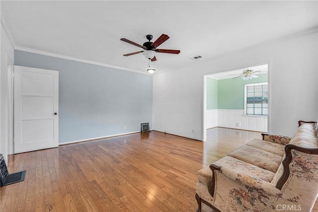 living room with light wood-style flooring, visible vents, a ceiling fan, and wainscoting