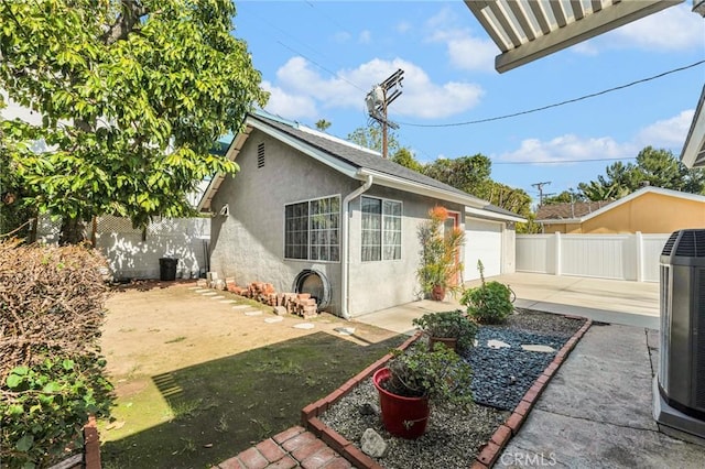 exterior space featuring driveway, central AC unit, a fenced backyard, and stucco siding